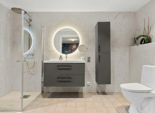 Baño con mueble de lavabo suspendido gris, espejo redondo con LED y columna alta
