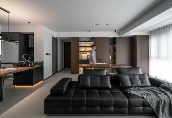 Salón abierto a la cocina con pared panelada en madera, hornacinas iluminadas y sofá de piel