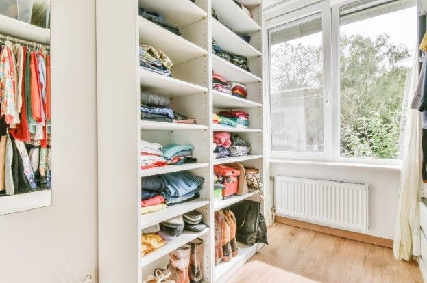 Vestidor con baldas abiertas y ropa ordenada junto a una ventana